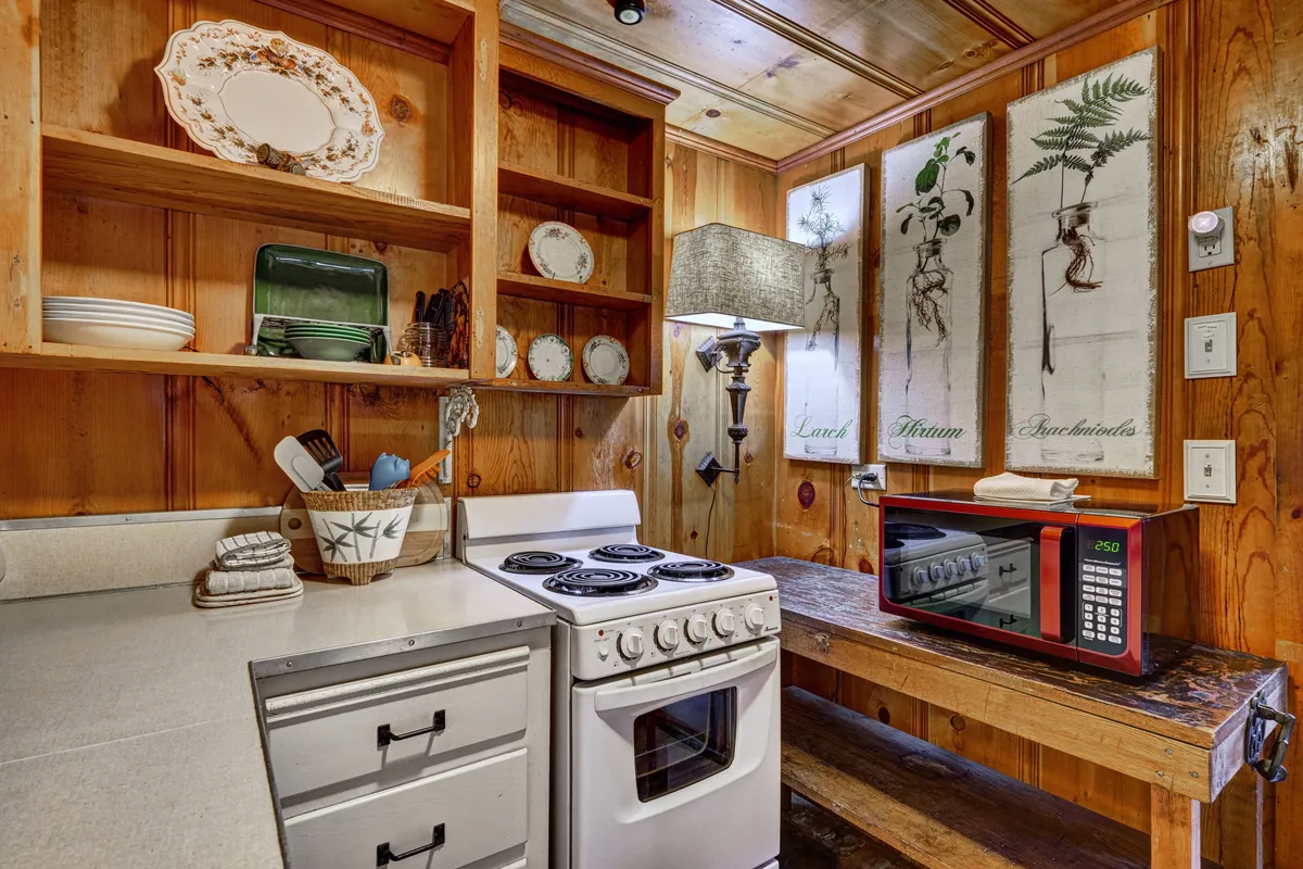 A cozy kitchen scene with a prominent stove and microwave, rustic wooden shelves, and carefully selected wall art. The space invites gatherings and culinary exploration, reflecting both heritage and present-day hospitality.